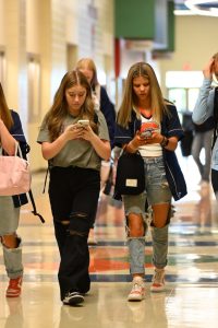 Freshmen Jorja Babb and Ansley Clayton walk down the hall on their phones. Currently, phones are allowed in the hallways but will be prohibited beginning in January. 